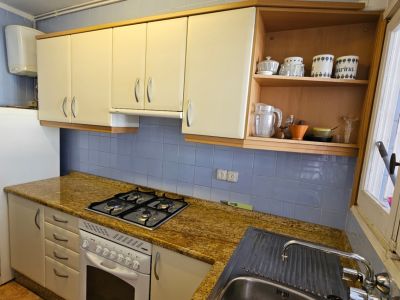 Cuisine fonctionnelle avec carrelage mural bleu, plan de travail en granit moucheté et armoires crème. Équipée d'une plaque de cuisson à gaz, four et évier en inox, éclairée par une fenêtre.