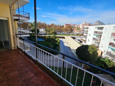 Grand balcon carrelé de terre cuite, avec vue sur le jardin commun, la piscine, les bâtiments résidentiels et une montagne lointaine sous un ciel clair.