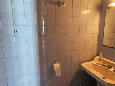 Salle de bain compacte avec carrelage mural carré bleu clair, réservoir de chasse haut à chaîne, lavabo sur colonne et plomberie apparente. Miroir et applique murale.