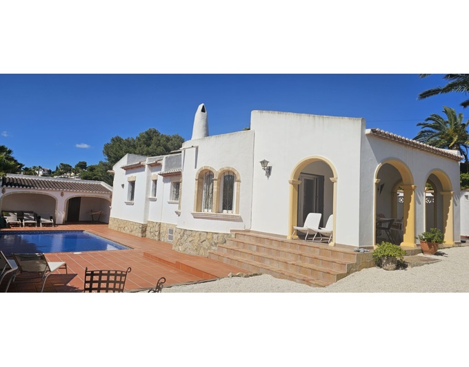 Extérieur de villa blanche de style méditerranéen, avec une terrasse couverte aux arches ocre et des escaliers en terre cuite. Piscine bleue et abri latéral visibles.