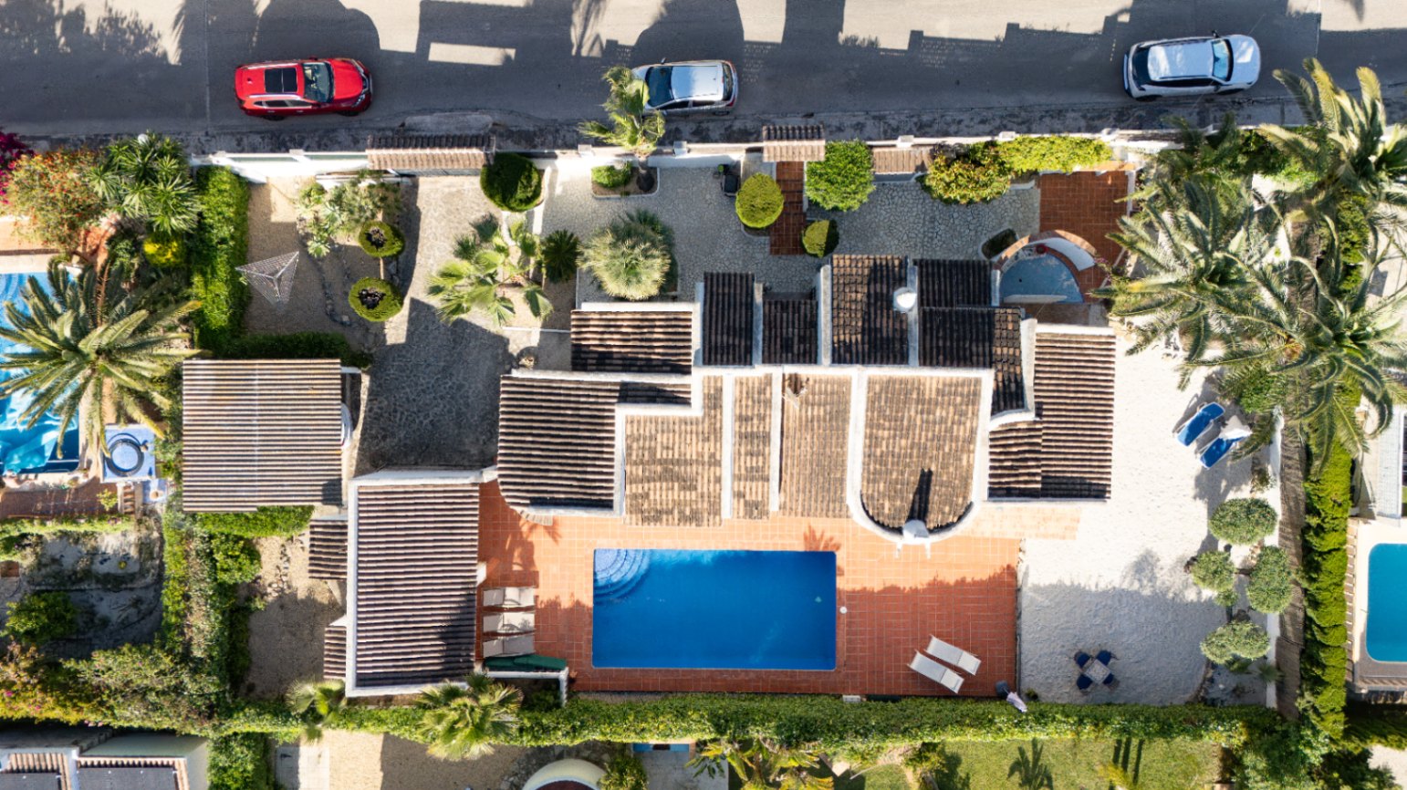 Vue aérienne de la villa privée avec piscine rectangulaire bleue, terrasse solarium en terre cuite et grand jardin arboré de plantes méditerranéennes et entrée pavée.