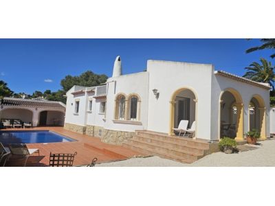 Extérieur de villa blanche de style méditerranéen, avec une terrasse couverte aux arches ocre et des escaliers en terre cuite. Piscine bleue et abri latéral visibles.