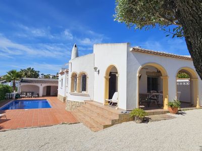 Extérieur de villa méditerranéenne blanche avec des arcs jaunes. La piscine carrelée en terre cuite et une terrasse couverte pour les repas extérieurs sont présentes.
