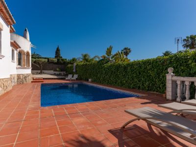 Piscine rectangulaire aux carreaux bleus sur une terrasse en terre cuite avec transats. Une haute haie verte et la villa blanche encadrent cet espace extérieur privé.