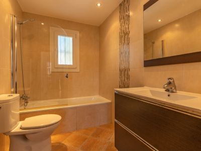 Salle de bain lumineuse avec baignoire et paroi vitrée, meuble-lavabo aspect bois foncé avec vasque blanche, et carrelage mural beige avec bande mosaïque décorative.