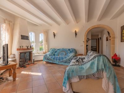 Salon lumineux avec cheminée traditionnelle en briques, fenêtres cintrées à barreaux et plafond à poutres apparentes. Le sol carrelé de terre cuite et une arche en pierre mènent à l'intérieur.