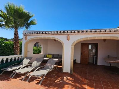 Vaste terrasse de piscine carrelée en terre cuite, trois chaises longues et une naya couverte avec salon extérieur et toilettes intégrées.