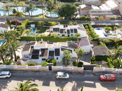 Vue aérienne de la villa privée à Javea, avec sa façade blanche, ses toits sombres, une grande piscine et un jardin méditerranéen luxuriant avec palmiers et entrée privée.