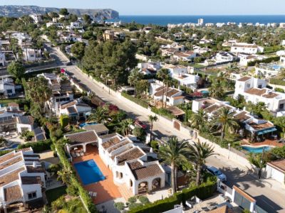 Vue aérienne du quartier résidentiel paisible de Javea, présentant de nombreuses villas blanches avec piscines privées, jardins méditerranéens luxuriants et la mer bleue au loin.