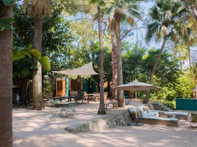 Vaste patio jardin tropical offrant plusieurs espaces de sièges ombragés sur gravier, dont une grande table à manger sous une voile avec guirlandes lumineuses et un coin salon rembourré.