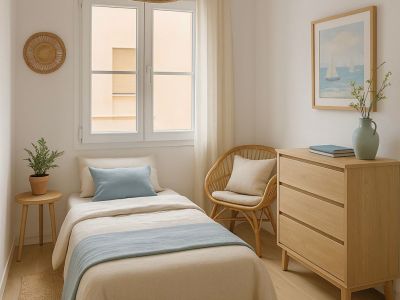 Chambre individuelle avec lit aux tons neutres et bleus. Présente un mobilier en bois clair et rotin, une suspension tressée et une lumière naturelle abondante.