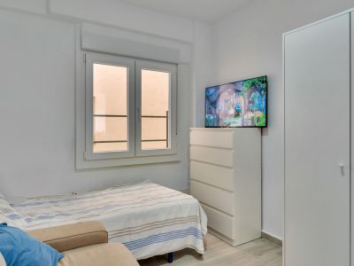 Chambre secondaire avec un lit simple, une armoire intégrée blanche et une commode surmontée d'une télévision. La fenêtre à double battant apporte de la lumière naturelle.