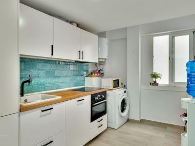Cuisine moderne avec armoires blanches, plan de travail en bois clair et crédence en carreaux turquoise à motifs. Équipée d'appareils intégrés et d'un espace buanderie avec lave-linge.