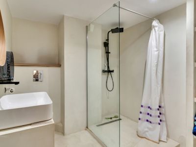 Salle de bain moderne avec lavabo vasque, robinetterie noire mate et douche à l'italienne avec paroi vitrée. Miroir en bois distinctif et étagères intégrées.
