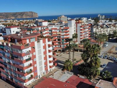 Vue aérienne du complexe résidentiel avec façades blanches, balcons rouge-orange, palmiers et la mer Méditerranée en arrière-plan.