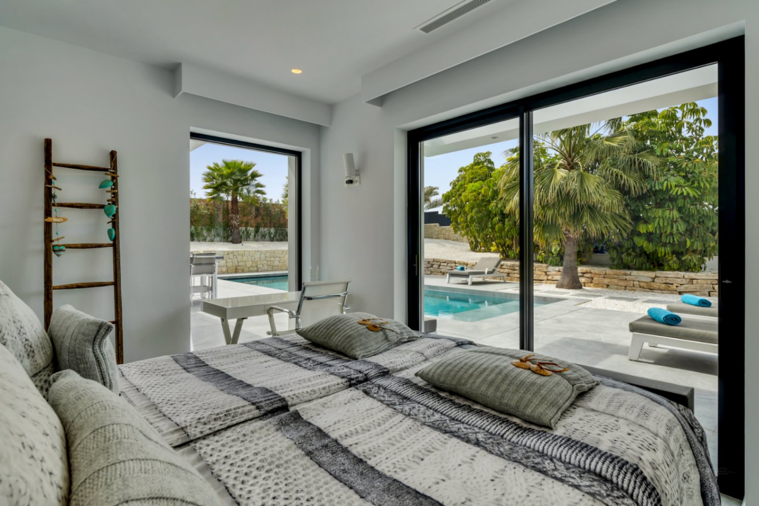 Chambre lumineuse avec accès direct à la piscine privée et aux transats via de grandes baies vitrées coulissantes. Design moderne aux murs blancs et lumière naturelle.