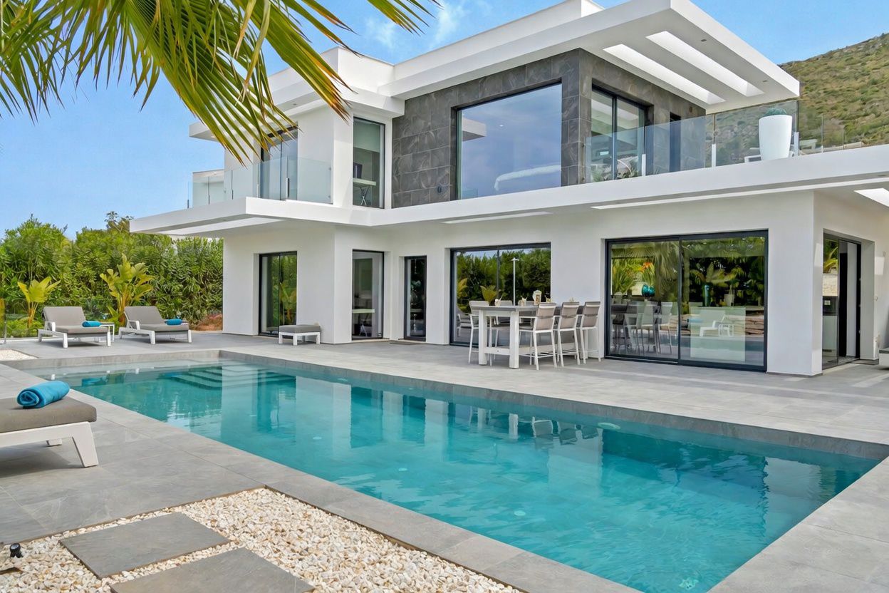 Extérieur de villa moderne avec piscine rectangulaire et vaste terrasse carrelée. De grandes baies vitrées relient l'intérieur, avec un espace repas extérieur et des vues sur la montagne.
