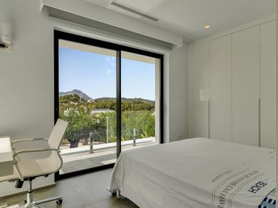 Chambre lumineuse avec de grandes portes coulissantes en verre s'ouvrant sur une terrasse et des vues sur les collines verdoyantes. Comprend des placards intégrés blancs et un bureau.