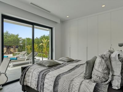 Chambre moderne avec de grandes portes coulissantes en verre donnant sur une terrasse privée avec transats et végétation méditerranéenne luxuriante. Placards intégrés discrets.