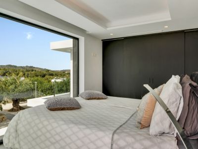 Chambre moderne avec une fenêtre du sol au plafond offrant une vue panoramique sur les collines verdoyantes. Des armoires encastrées sombres et un éclairage discret complètent l'espace.