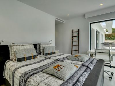 Chambre principale moderne avec lit double, accès direct à une terrasse extérieure et espace de travail intégré. Éclairage encastré et échelle décorative visible.