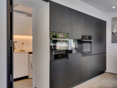 Cuisine moderne avec armoires foncées grain de bois, appareils Bosch intégrés et accès à une buanderie lumineuse avec machine à laver et robinet en cuivre.