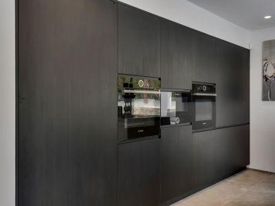 Cuisine moderne et épurée avec des armoires en bois foncé du sol au plafond et des appareils Bosch intégrés. Comprend un four et un micro-ondes encastrés, reflétant l'extérieur.