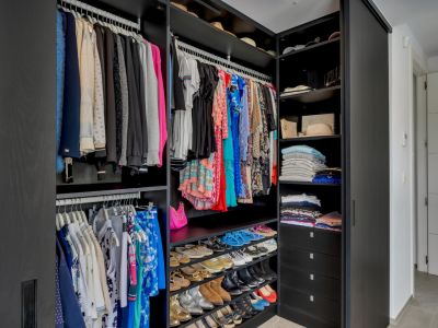 Dressing fonctionnel avec armoires sombres, multiples tringles de suspension, étagères ouvertes pour accessoires et rangements inclinés dédiés aux chaussures.