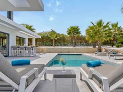 L'espace de vie extérieur moderne comprend une piscine rectangulaire, des transats confortables et un bar intégré avec tabourets hauts, agrémenté d'un aménagement paysager luxuriant de palmiers.