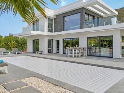 L'extérieur de la villa moderne présente une grande piscine couverte et une vaste terrasse carrelée avec coin repas et chaises longues. De larges baies vitrées et balcons avec garde-corps en verre.