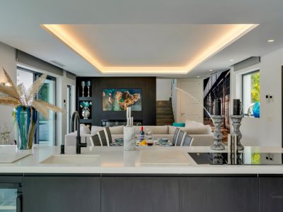 L'îlot de cuisine ouvert, avec plan de travail blanc et plaque intégrée, relie la salle à manger et le salon, accentué par un éclairage indirect élégant.