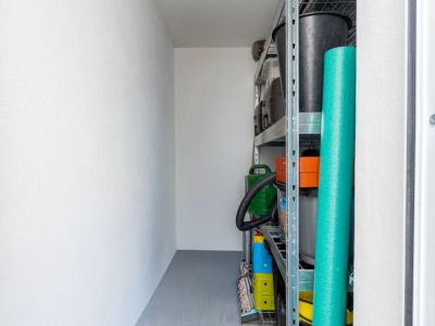 Pièce de rangement fonctionnelle avec murs blancs, sol gris et étagères métalliques robustes pour divers articles ménagers.
