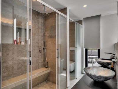 Salle de bain contemporaine avec douche à l'italienne vitrée, banc intégré et carrelage texturé. Double vasque en verre sur meuble sombre, vue sur un espace extérieur.