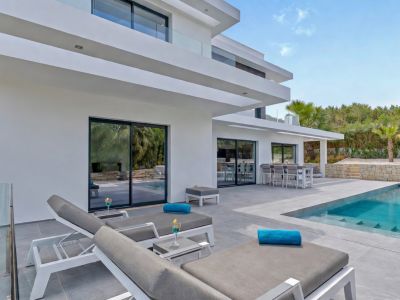 Vaste terrasse extérieure de la villa moderne, comprenant une piscine rectangulaire, des chaises longues contemporaines et un espace repas élégant, accessible par de grandes baies vitrées.