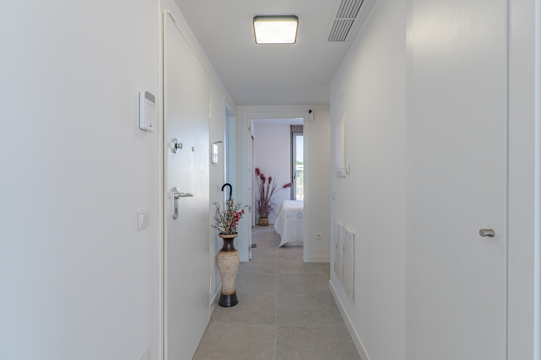 Couloir moderne et lumineux avec carrelage gris clair et murs blancs. Doté d'un panneau de sécurité, d'un plafonnier contemporain et d'une vue sur une chambre.