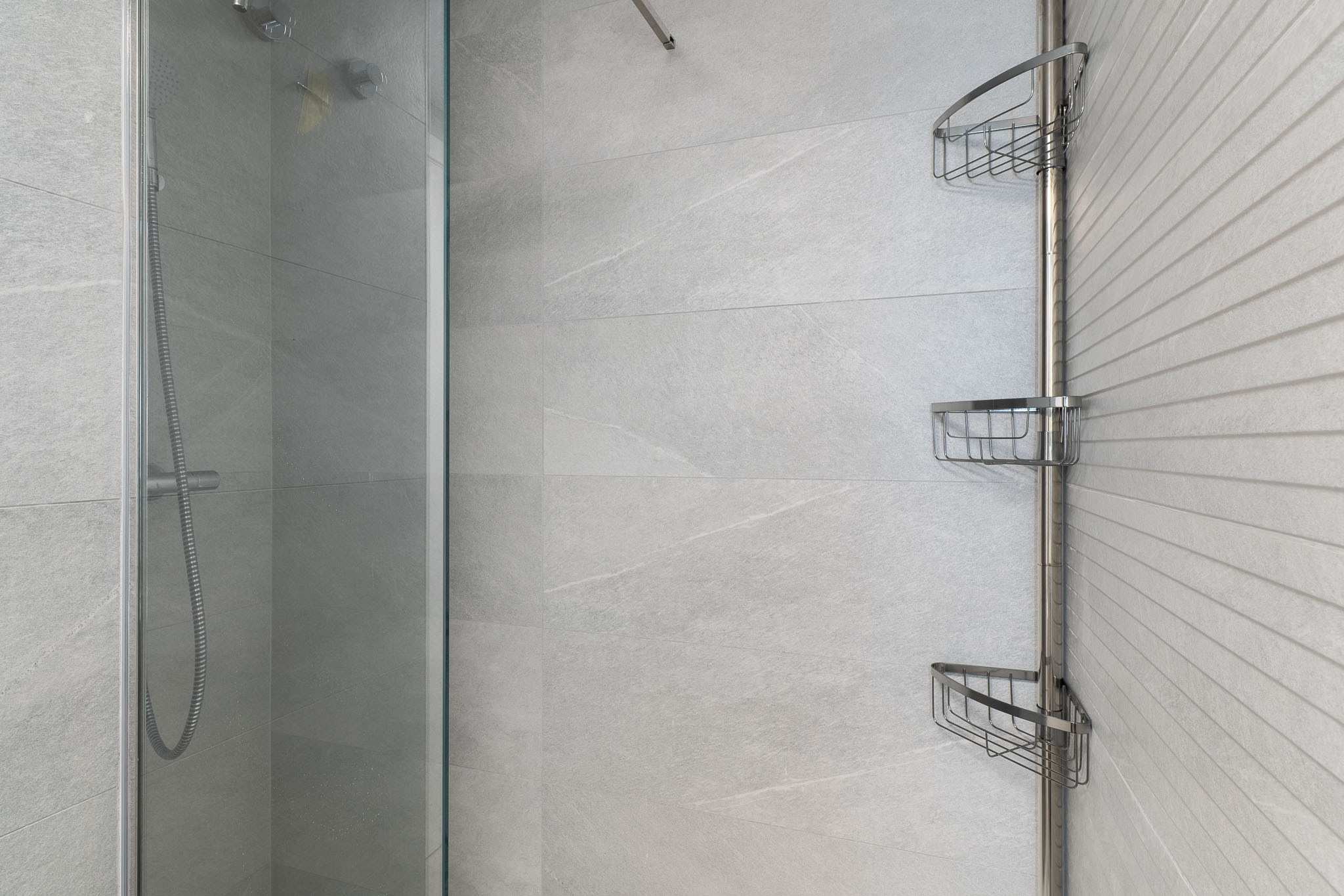 Espace douche contemporain avec carrelage gris clair grand format, un mur d'accent texturé, paroi vitrée et une étagère d'angle chromée pratique.