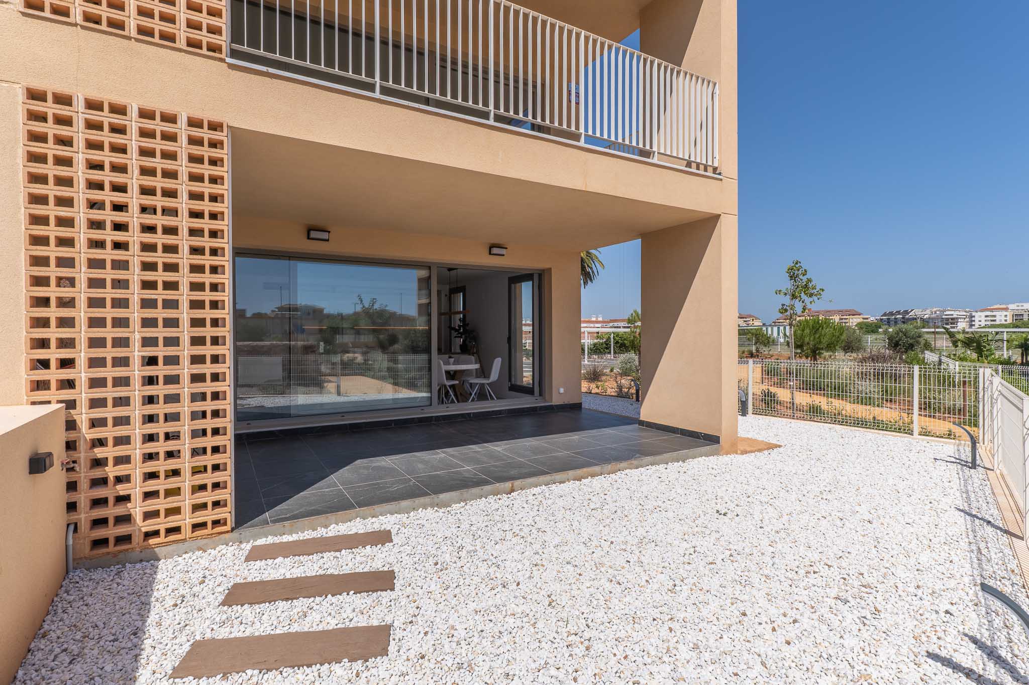 Terrasse couverte en rez-de-chaussée avec carrelage foncé, donnant sur un jardin privé de gravier blanc. De grandes baies vitrées révèlent un espace repas lumineux, agrémenté d'une façade en briques décoratives.