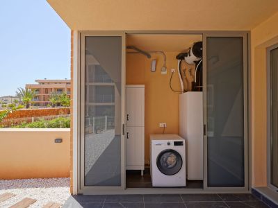 Buanderie extérieure avec machine à laver Bosch et système aérothermique, accessible depuis une terrasse carrelée avec galets décoratifs et vue sur jardin.