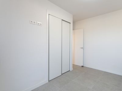 Chambre avec un grand placard intégré à portes coulissantes blanches et un sol carrelé gris clair. Des prises électriques et de données sont installées.