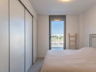 Chambre lumineuse avec placard intégré à portes coulissantes blanches, sol carrelé et accès direct à l'extérieur par une porte vitrée. Lit avec tête de lit capitonnée.