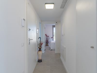Couloir moderne et lumineux avec carrelage gris clair et murs blancs. Doté d'un panneau de sécurité, d'un plafonnier contemporain et d'une vue sur une chambre.