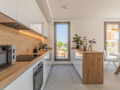 Cuisine ouverte moderne avec des armoires blanches laquées, des plans de travail et crédence effet bois, et un éclairage LED sous les meubles. Équipée d'appareils intégrés et ouvrant sur l'extérieur.