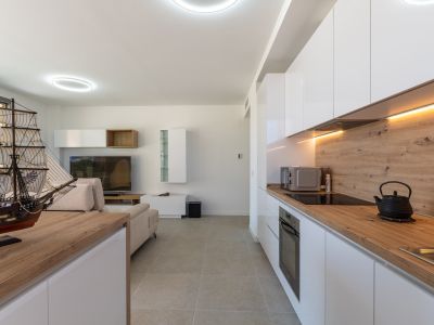 Espace de vie ouvert intégrant un salon et une cuisine moderne. La cuisine présente des armoires laquées blanches, des plans de travail effet bois clair, des appareils intégrés et un éclairage LED sous les meubles.