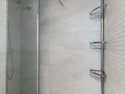 Espace douche contemporain avec carrelage gris clair grand format, un mur d'accent texturé, paroi vitrée et une étagère d'angle chromée pratique.