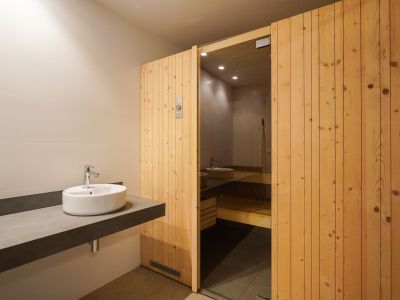Espace vestiaire avec un lavabo vasque design sur meuble flottant et l'entrée du sauna, dotée d'une porte en bois à lattes et d'un panneau vitré.