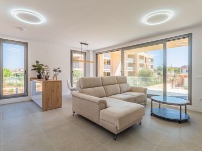 Lumineux salon-salle à manger ouvert, avec canapé sectionnel beige et table basse ovale. Grandes baies vitrées offrent lumière naturelle et vues résidentielles. Cuisine ouverte avec comptoir en bois.