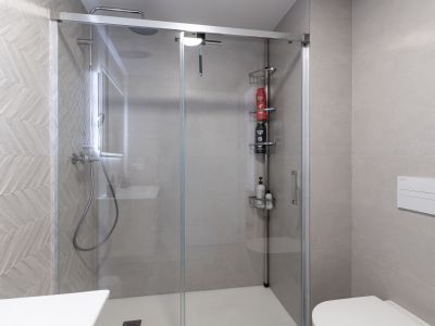 Salle de bain moderne avec cabine de douche vitrée et receveur blanc. Le mur de la douche présente un carrelage gris à motif chevron, complété par une douche à effet pluie et des WC suspendus.