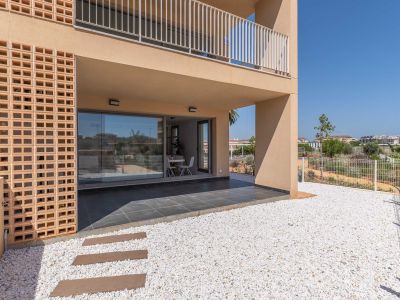 Terrasse couverte en rez-de-chaussée avec carrelage foncé, donnant sur un jardin privé de gravier blanc. De grandes baies vitrées révèlent un espace repas lumineux, agrémenté d'une façade en briques décoratives.