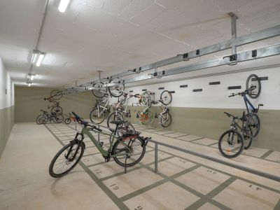Vaste espace de stationnement commun pour vélos avec emplacements numérotés au sol et supports muraux. Éclairé par des néons, il offre un rangement sécurisé au sein du complexe résidentiel.