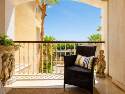 Agréable terrasse privée avec un fauteuil en osier foncé, sol en marbre clair et une balustrade ornée. Agrémentée de jardinières en pierre, elle offre des vues sur les palmiers et un ciel azur.